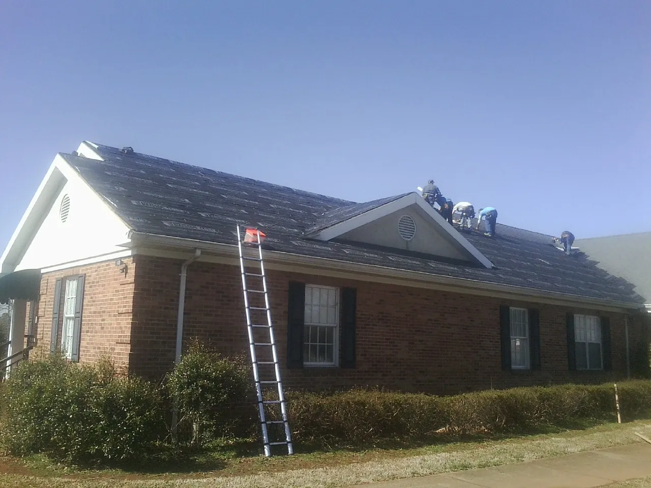 Crew tearing shingles off a brick ranch roof with a ladder set — Emergency Roof Repair work by our crew in Elko New Market