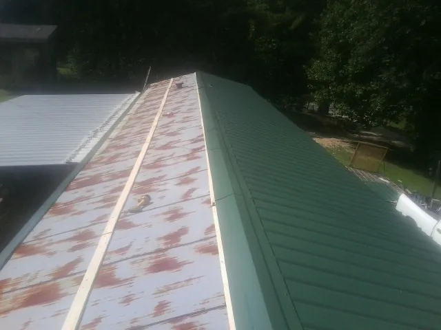 Old rusted panels beside newly installed green metal roofing — Wind Damage Roof Repair by Roofing Brothers in Elko New Market