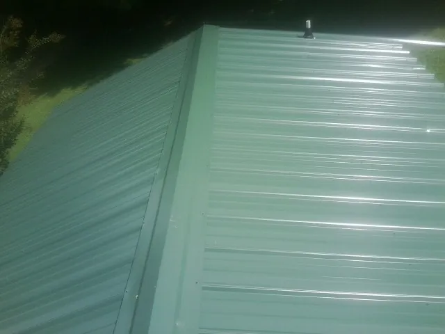 New green metal panels meeting at the ridge of a roof — Flat Roof Repair work by our crew in Elko New Market