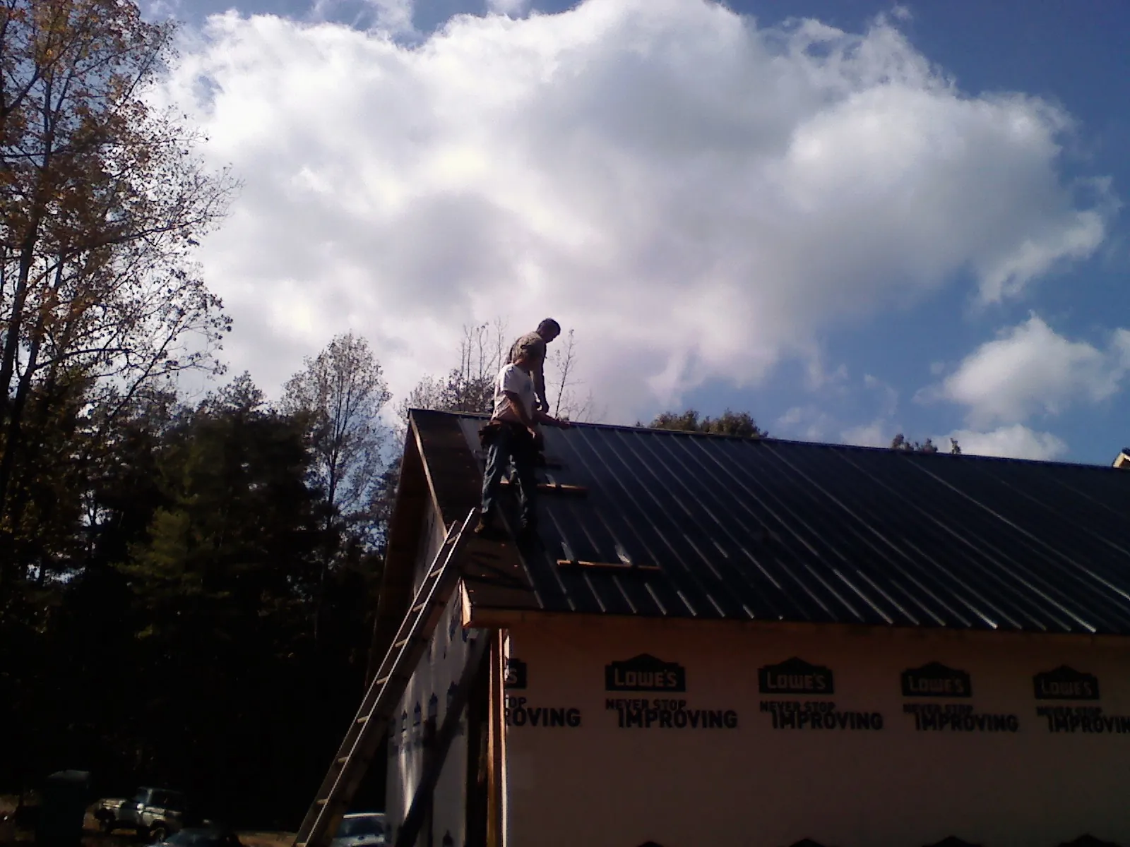 Roofer fastening dark metal panels high against a cloudy sky, from a Roof Inspection job in Elko New Market
