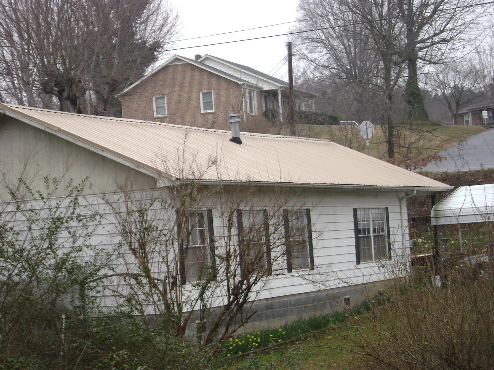 Tan metal roof on a white sided house set into a hillside — Commercial Roofing by Roofing Brothers in Elko New Market