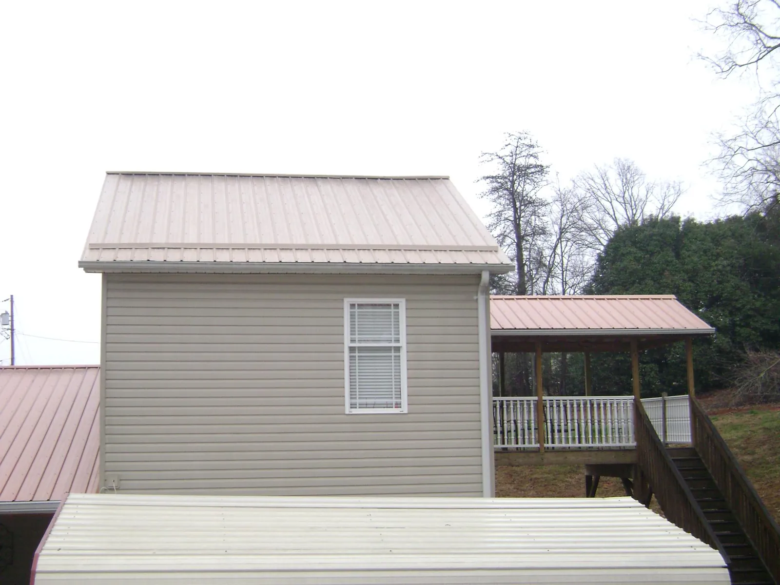 Tan metal roofs on a two story addition and attached porch, from a Roof Replacement job in Elko New Market